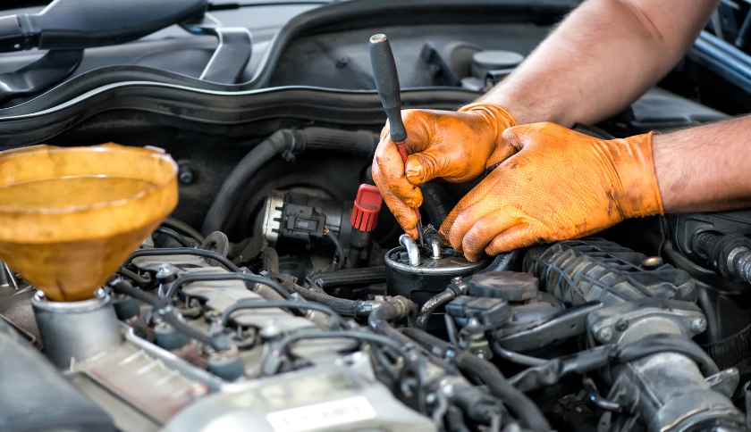 Mecânico com luvas de proteção fazendo manutenção no motor de um carro